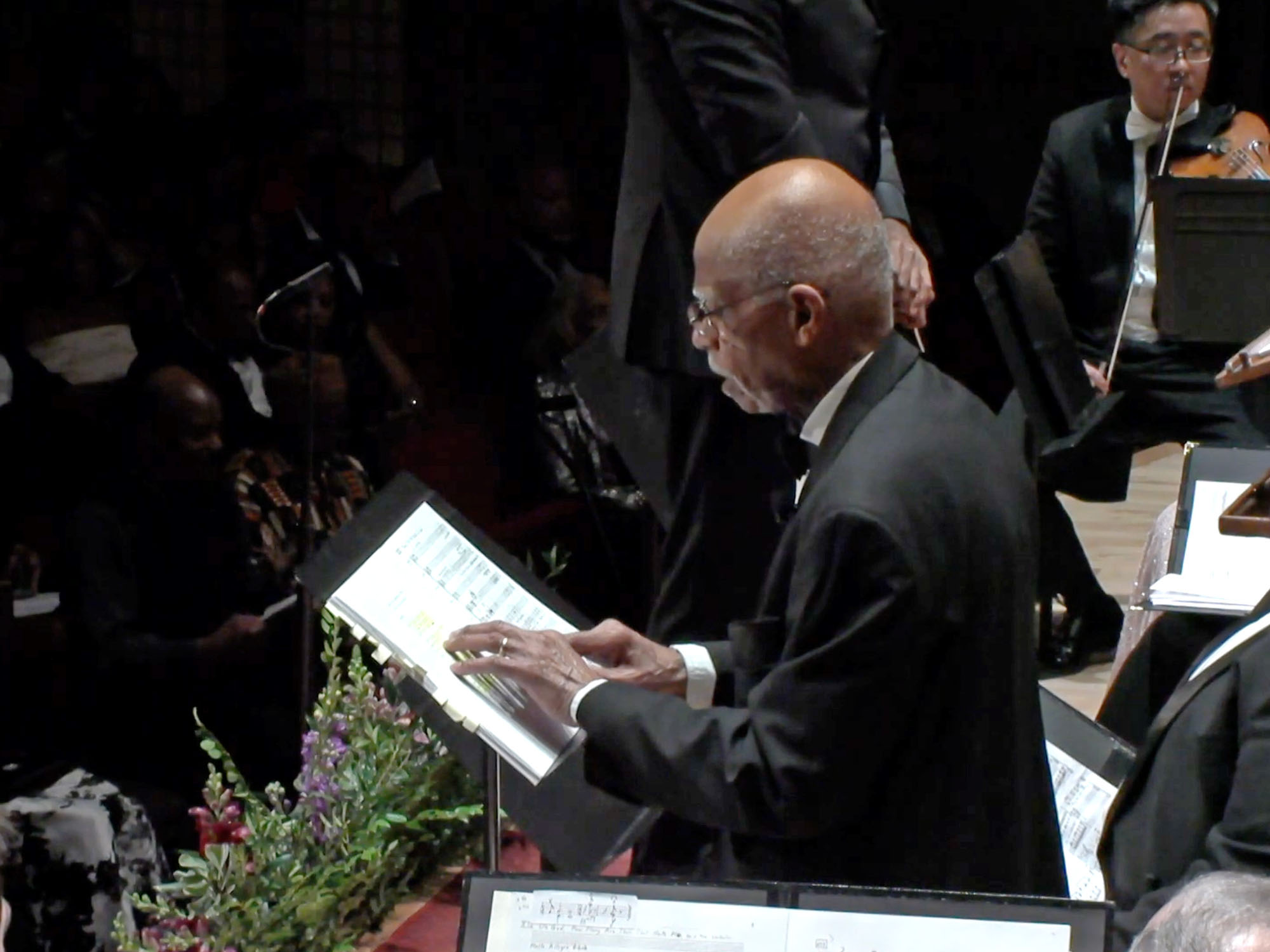 Gershwin A House of Many Mansions featured During a performance of Undine Smith Moore's Scenes from the Life of a Martyr with other performers (including Detroit Symphony Orchestra) on stage, George Shirley presents while referencing sheets on a music stand.