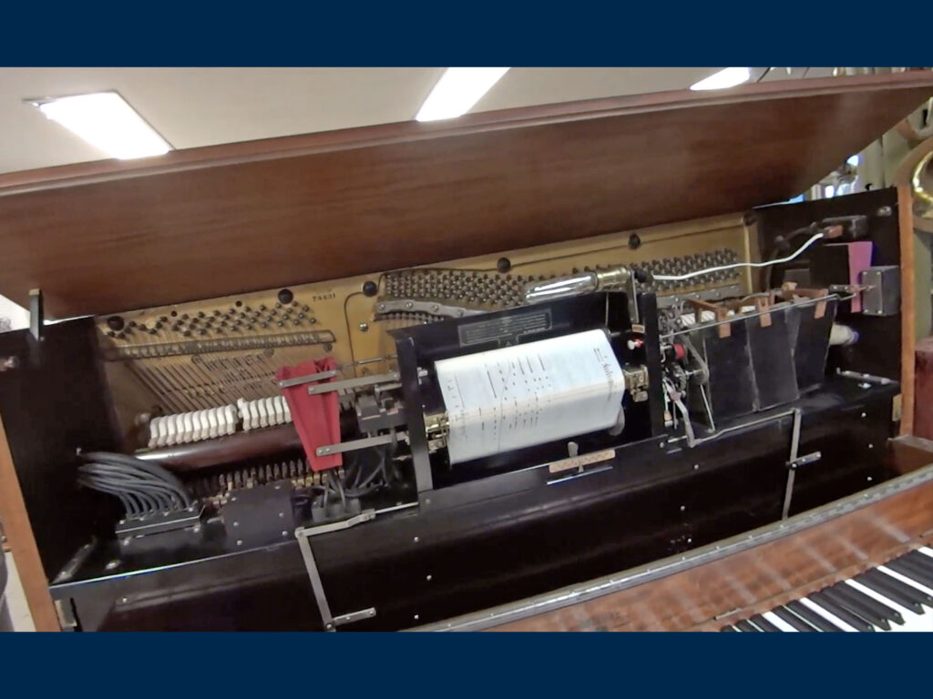 A piano roll plays on an upright piano with its lid open.