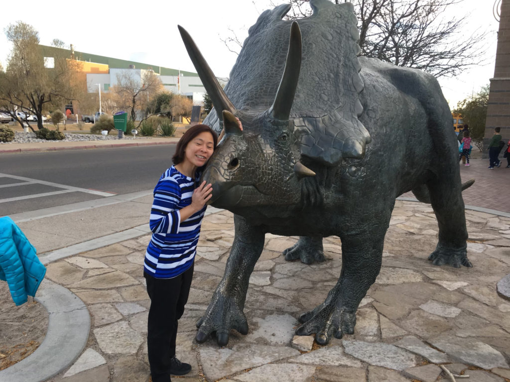Christi-Anne Castro standing next to a large metal statue of a triceratops in Albuquerque