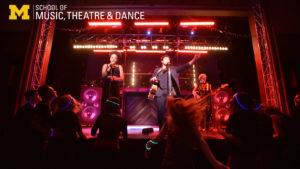 Zoom background - Musical Theatre performance of One Hit Wonder - showing a scene of a rock concert with singers, audience, and stage lights