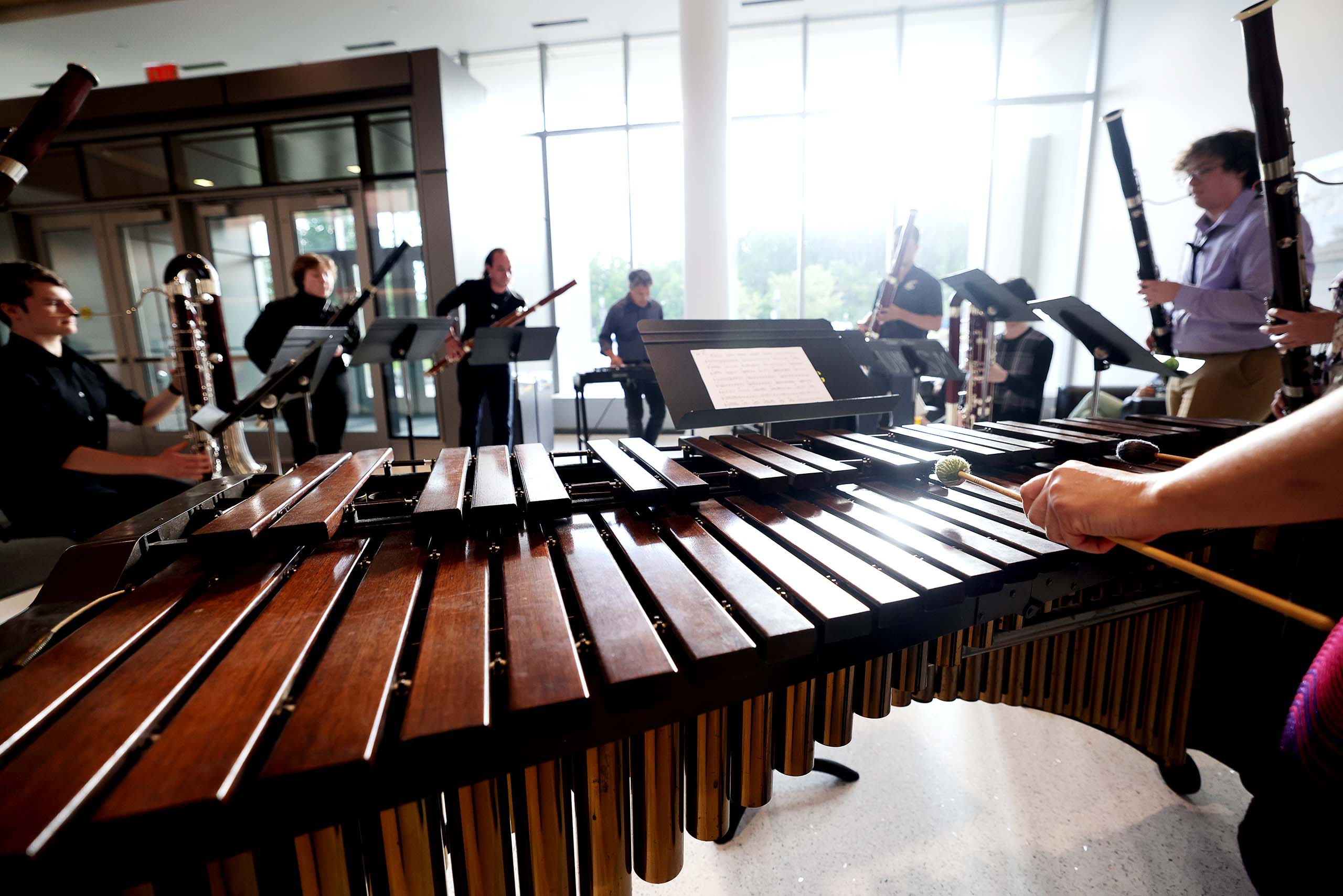 A circle of bassoonists perform with a marimba player in Brehm Atrium, as sunlight streams in the windows.