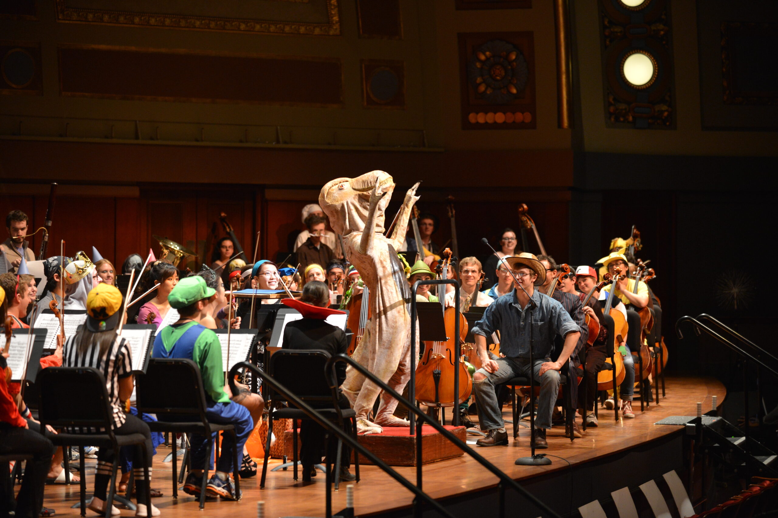 An orchestra dressed in Halloween costumes, with a T-Rex as conductor
