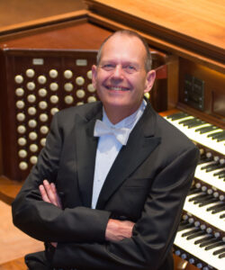 James Kibbie, smiling and wearing tuxedo, seated in front of Frieze Memorial Organ in Hill Auditorium, Ann Arbor, Michigan