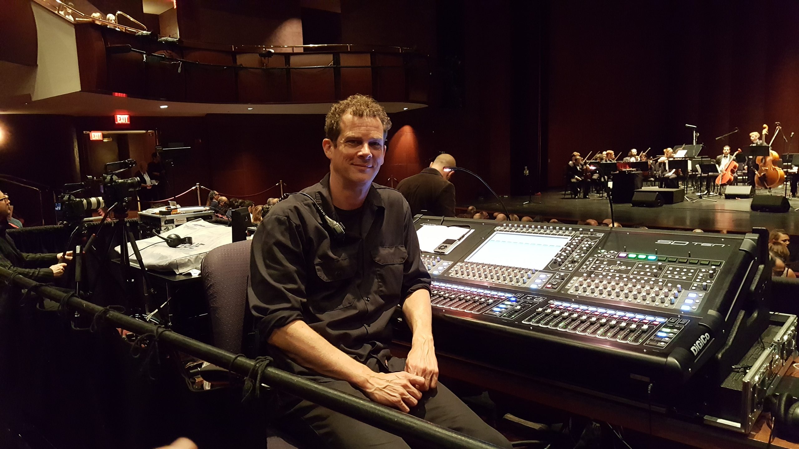 A man sits in front of mixing console in a concert hall.