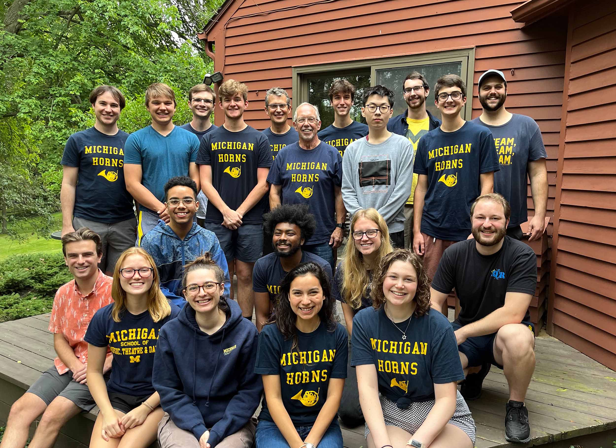 A group of 20 students and faculty poses outdoors, most of them wearing "Michigan Horns" t-shirts.