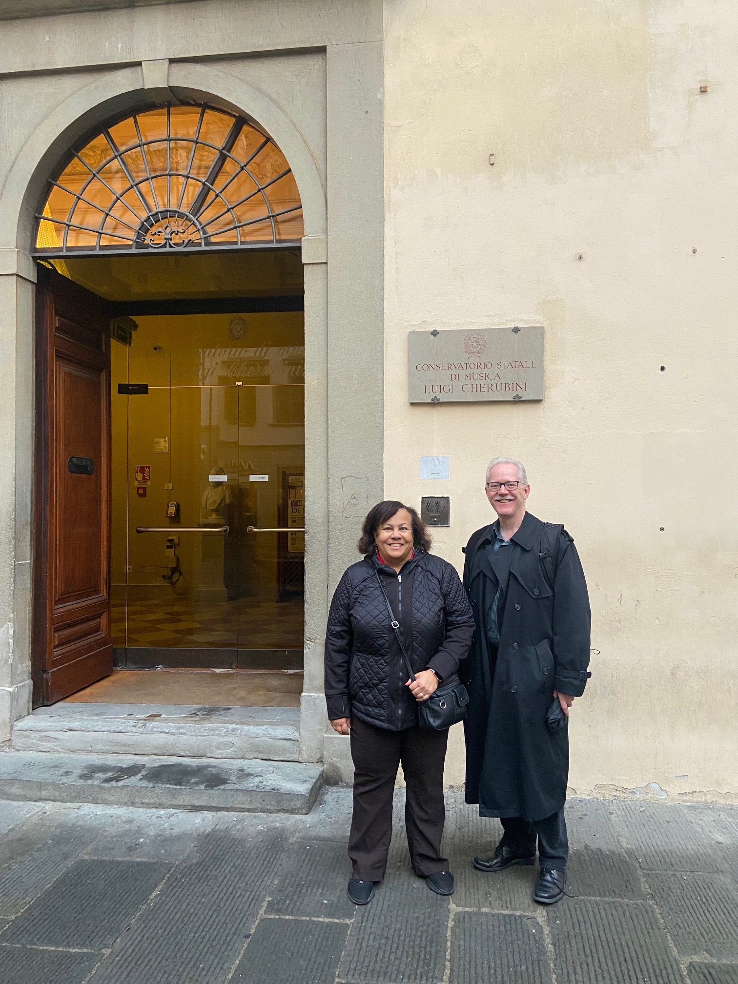 Woman and Man in black coats stand in front of conservatory door with a palladian arch