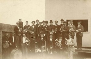 Old black and white photo of 23 band members in two rows, holding instruments and wearing suits and top hats.