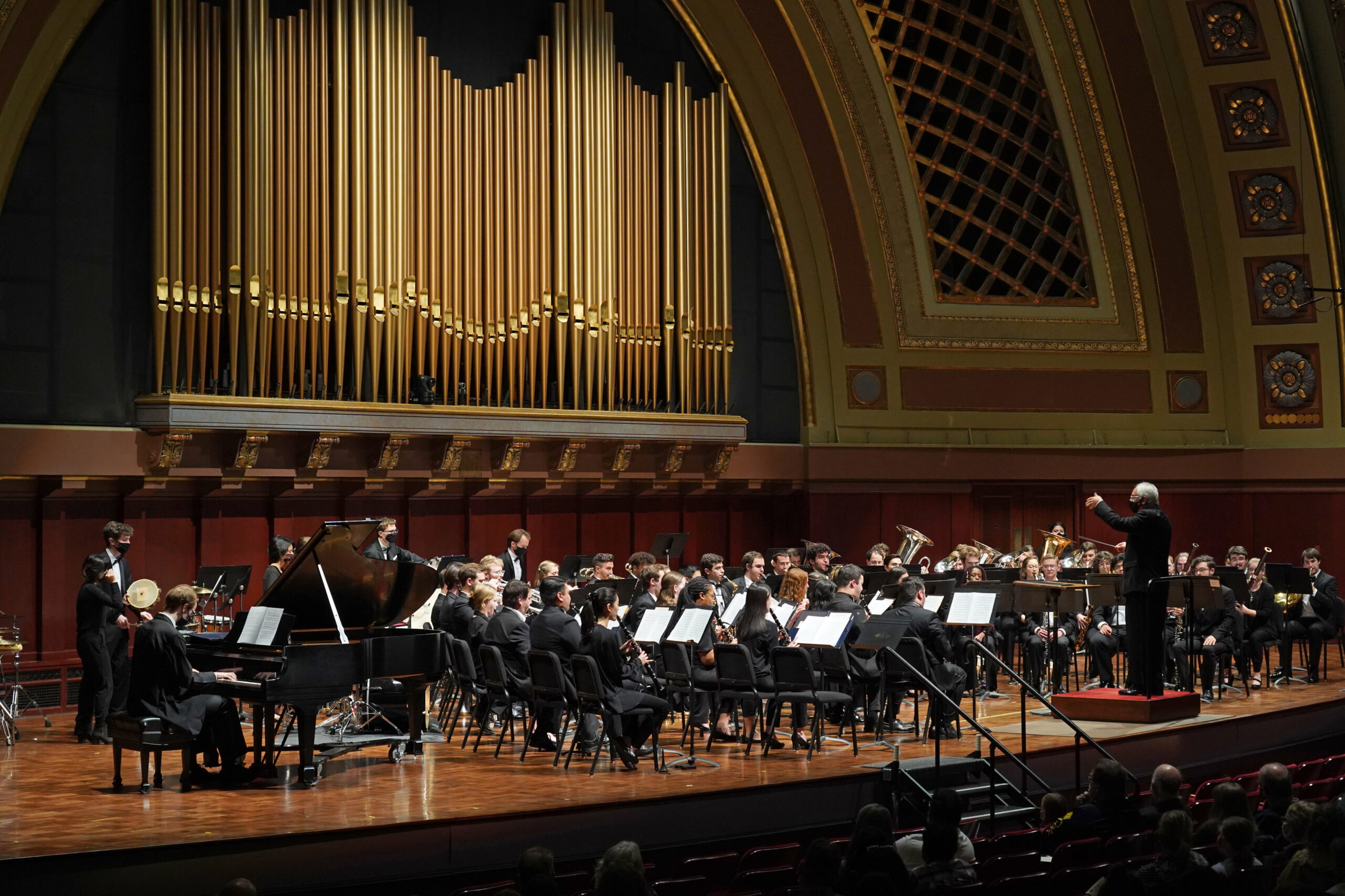 Symphony Band photographed during performance on the Hill Auditorium stage; the conductor's arm is raised.