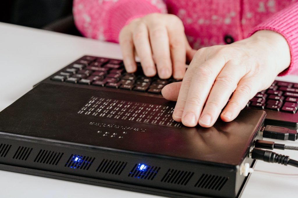 Two hands rest on a black keyboard and a black device with rows of dots.
