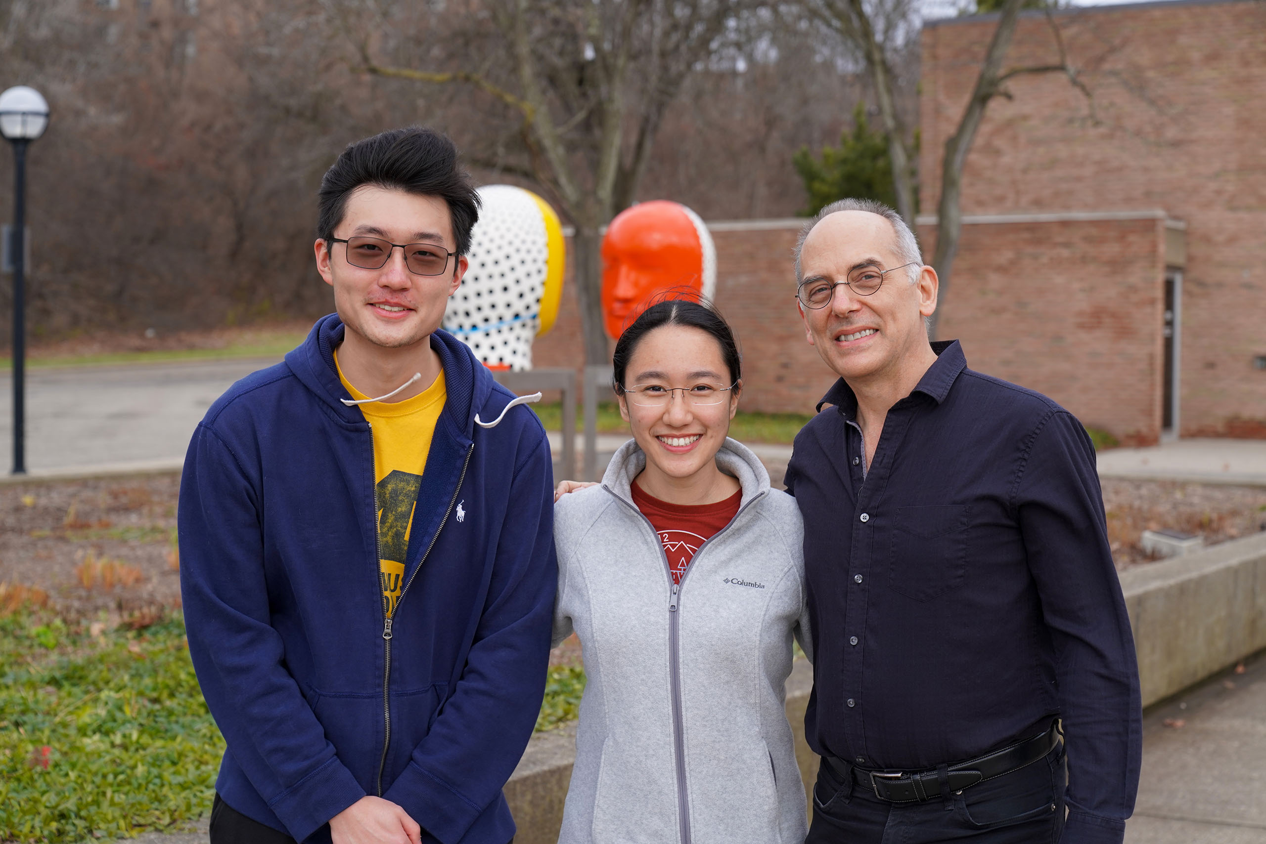 Three individuals smile and pose outside the Moore Building.