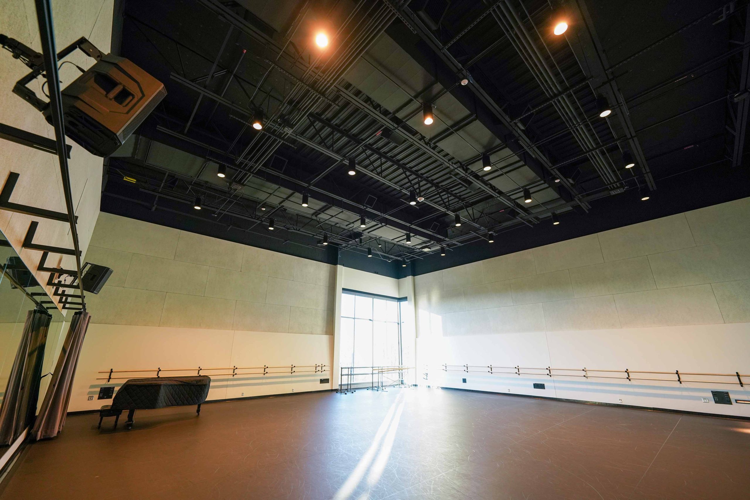 A dance studio with stone-like walls; light shines in from tall corner windows.