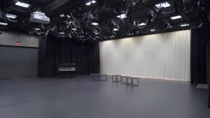 A large studio space with a ceiling full of equipment, a piano, and curtain backdrops.