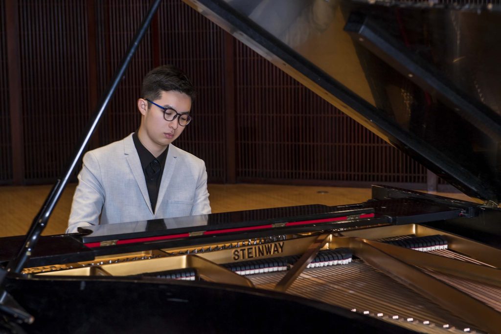 Zhengyi Huang pictured seated behind a grand piano.