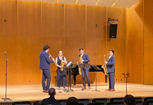 A saxophone quartet, wearing blue, performs on stage with an audience