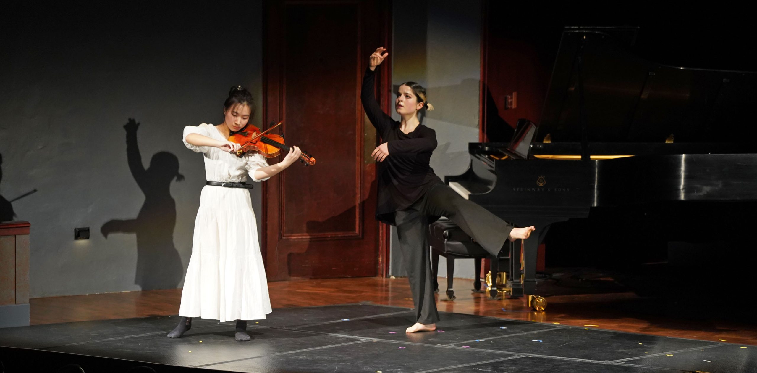 A violist wearing white and a dancer wearing black perform together on stage