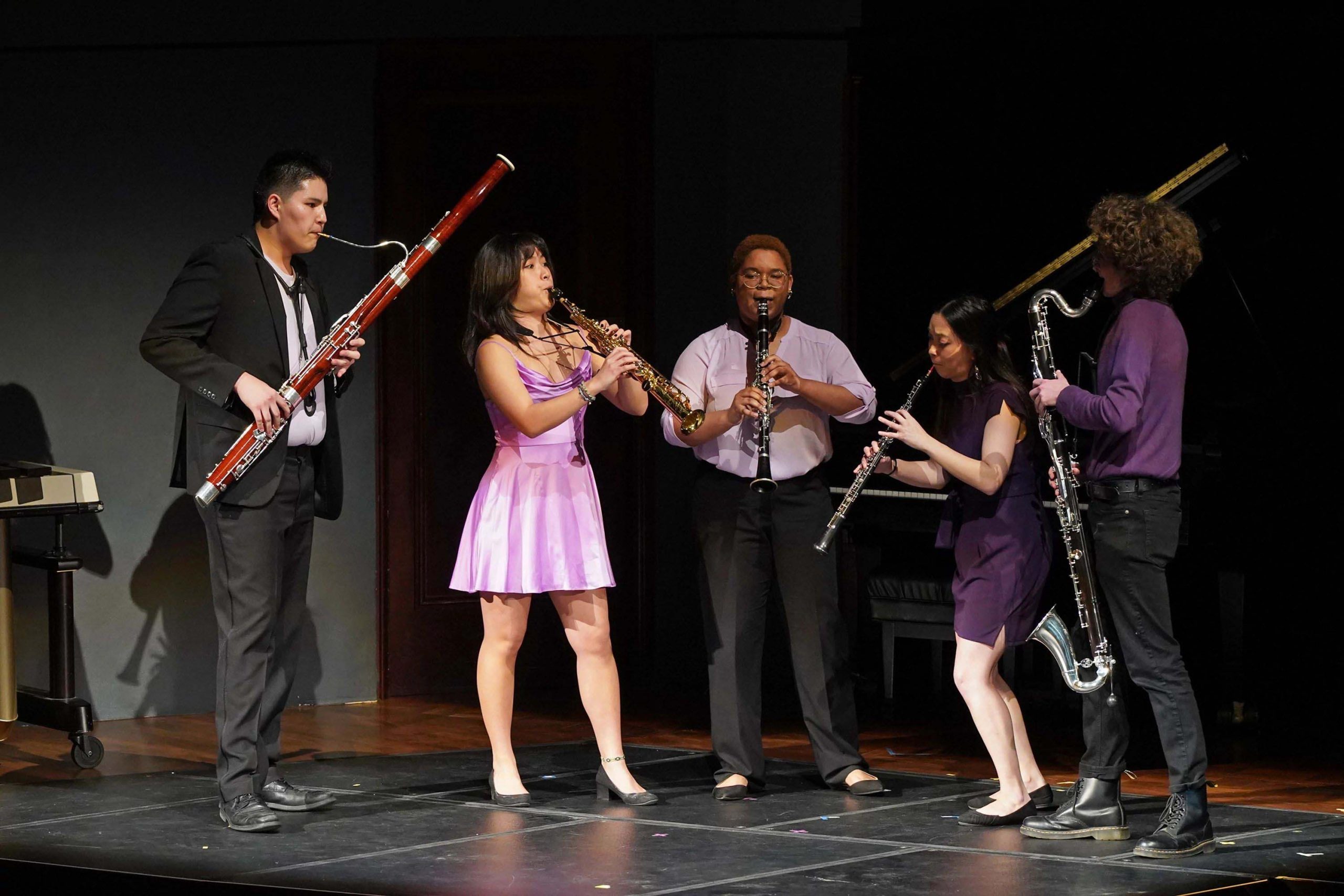 An ensemble of five wind players perform jazz music standing on stage