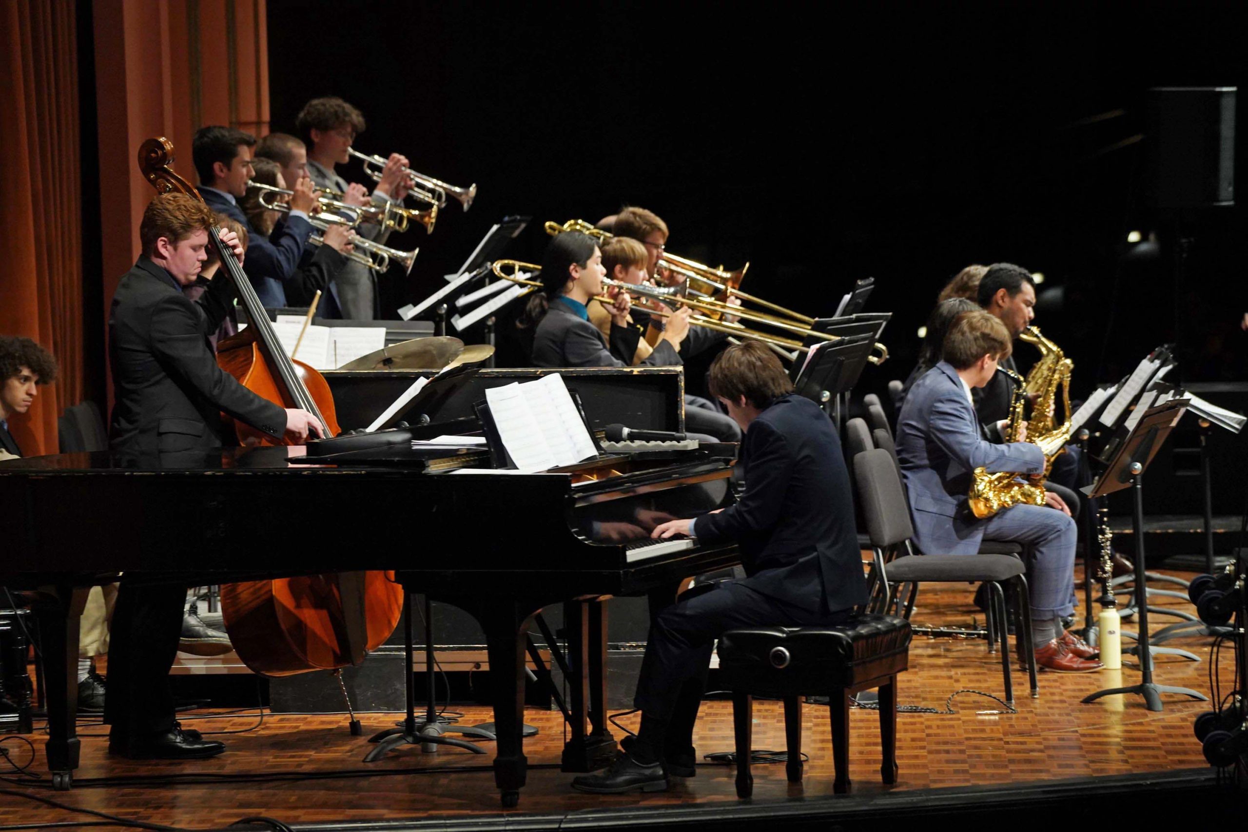 Pianist, bassist, and three rows of brass and wind players on stage at a Jazz Lab Ensemble performance