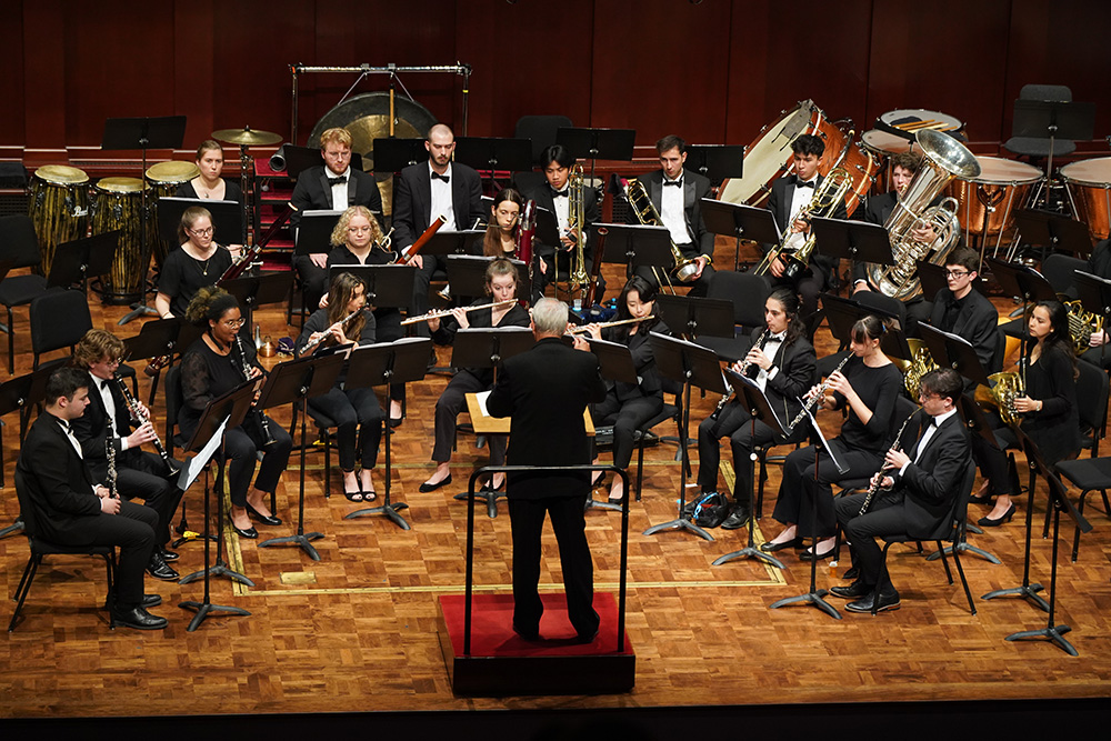 Detail of woodwinds and flutes playing with the Symphony Band on stage, the conductor's back at center