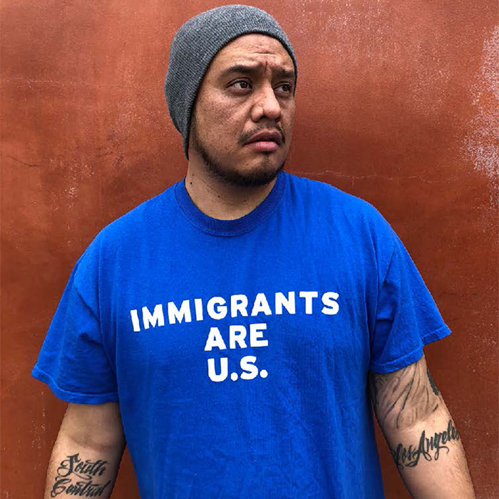 Alex Alpharaoh pictured wearing a blue t-shirt that says: Immigrants are U.S.