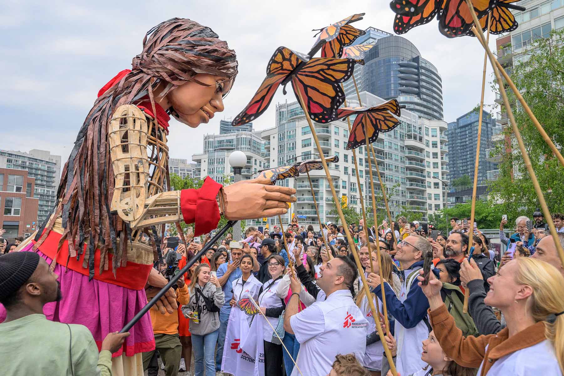 A crowd of people enjoy a display of large puppets in a city.