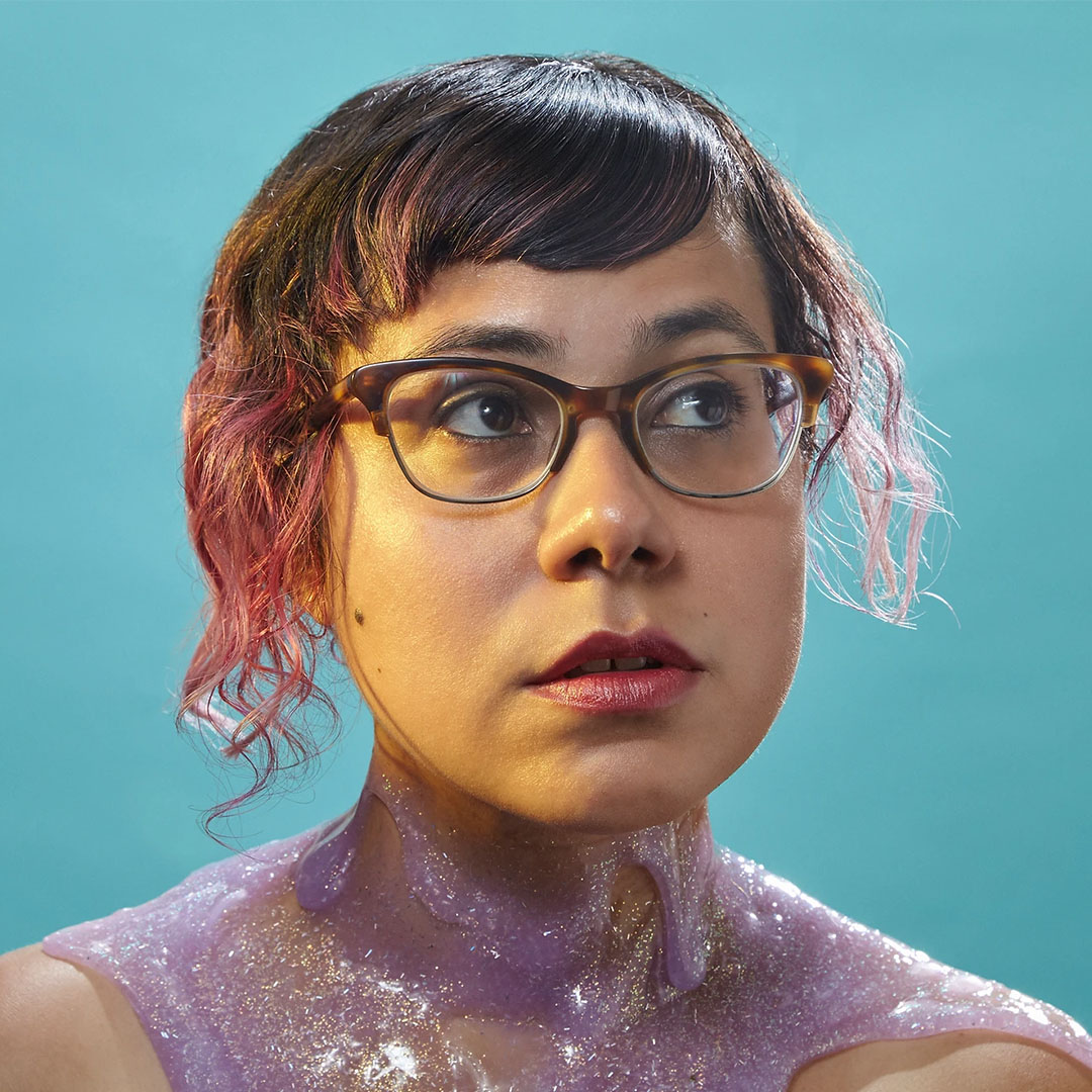 Angélica Negrón portrait with glasses; sparkly purple goo covers her neck and shoulders; teal background.