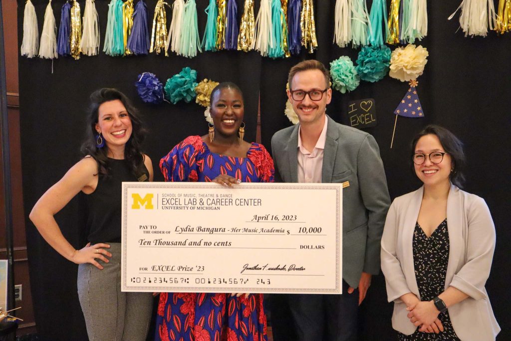 Four people pose smiling with a giant check for the $5,000 EXCEL Prize