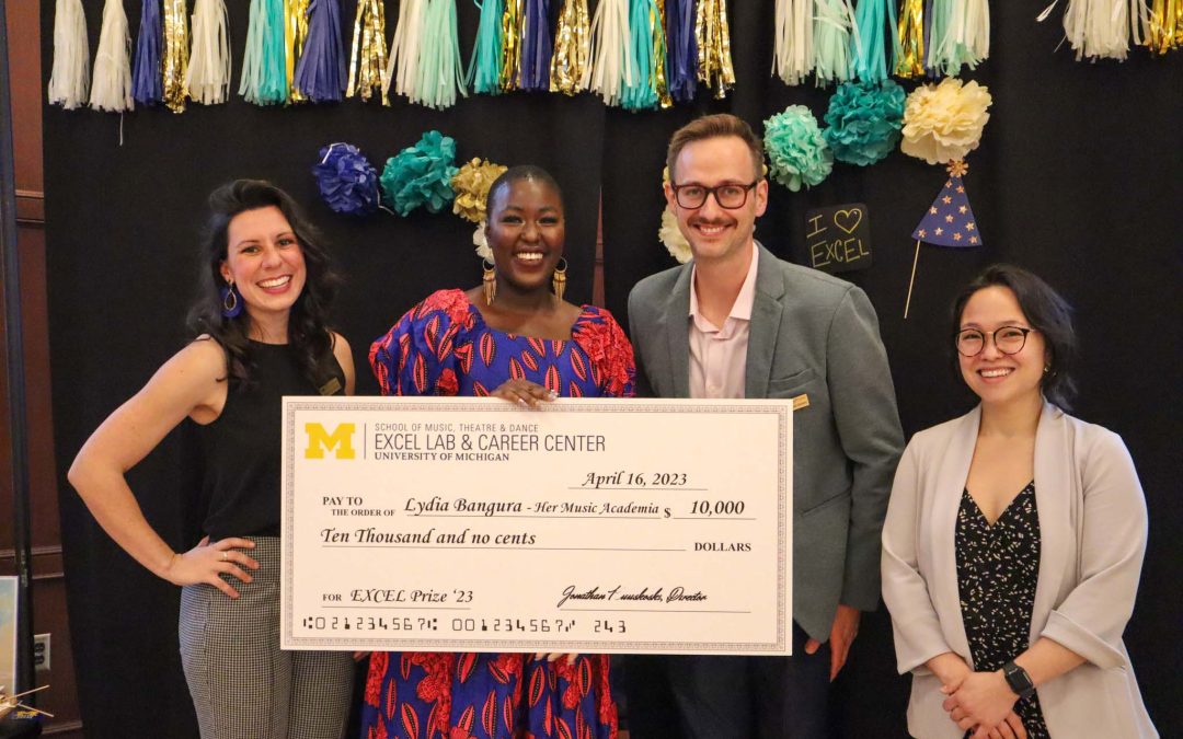 Four people pose smiling with a giant check for the $5,000 EXCEL Prize