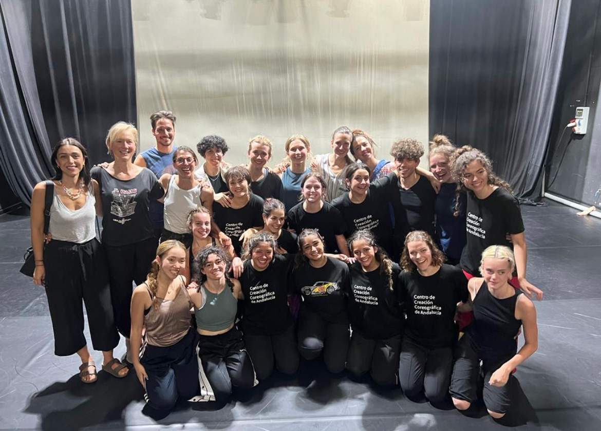 Two dozen smiling dancers, some with matching t-shirts, pose in a studio