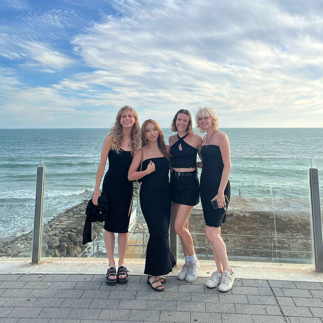 Four students in black attire pose with a waterfront.