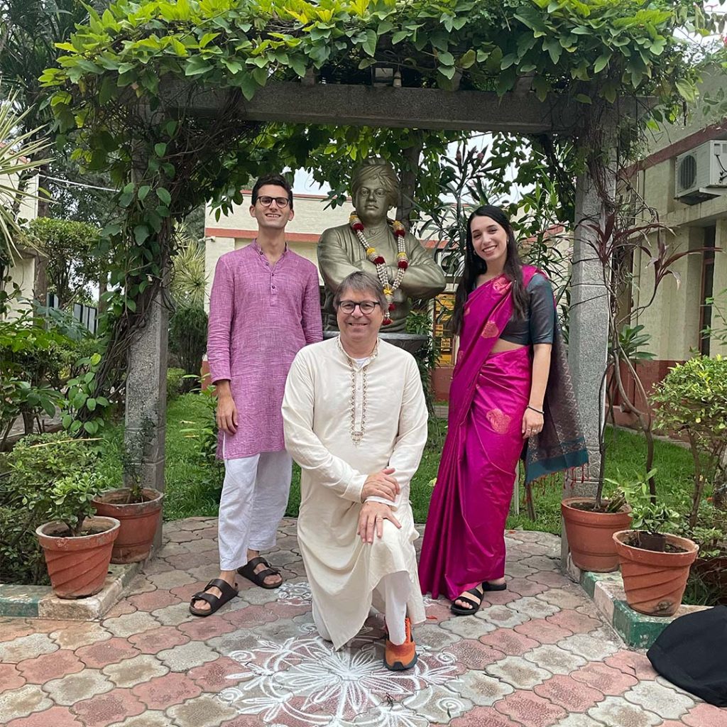 Three pose with a statue in a garden, wearing Indian style attire