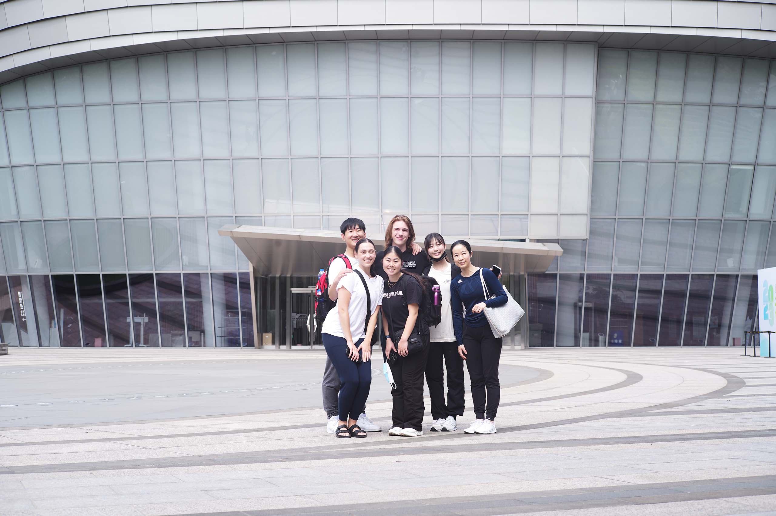 Six U-M travelers pose standing outside a grand modern building