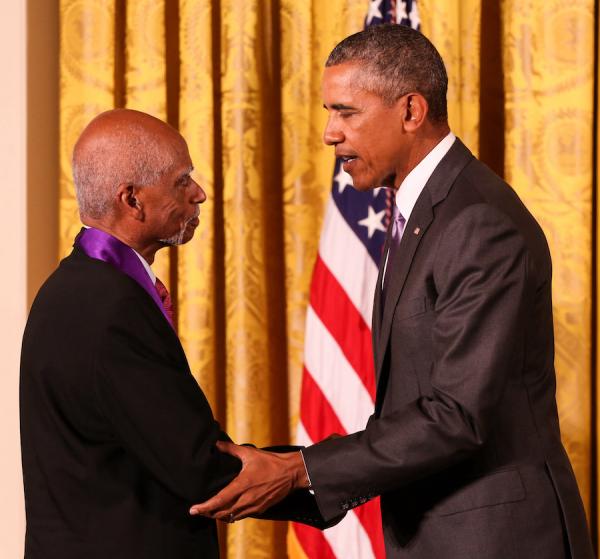 George Shirley and President Obama shake hands, standing in front of gold curtains and an American flag