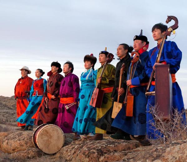 Nine people stand in a row, with traditional Mongolian attire and instruments  