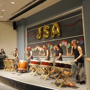 A row of Taiko drummers perform on a stage