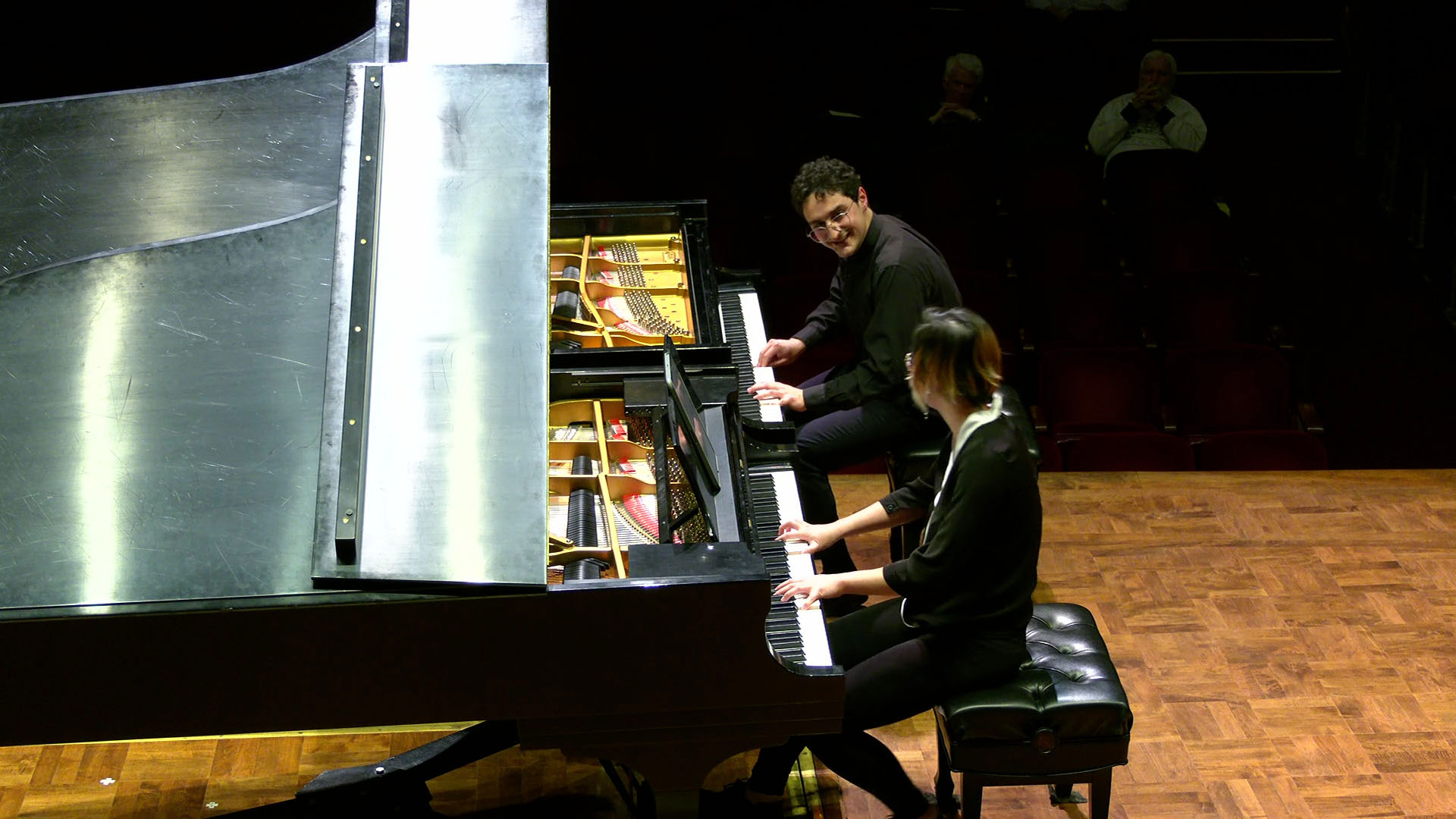 Two pianists play on side-by-side grand pianos on stage