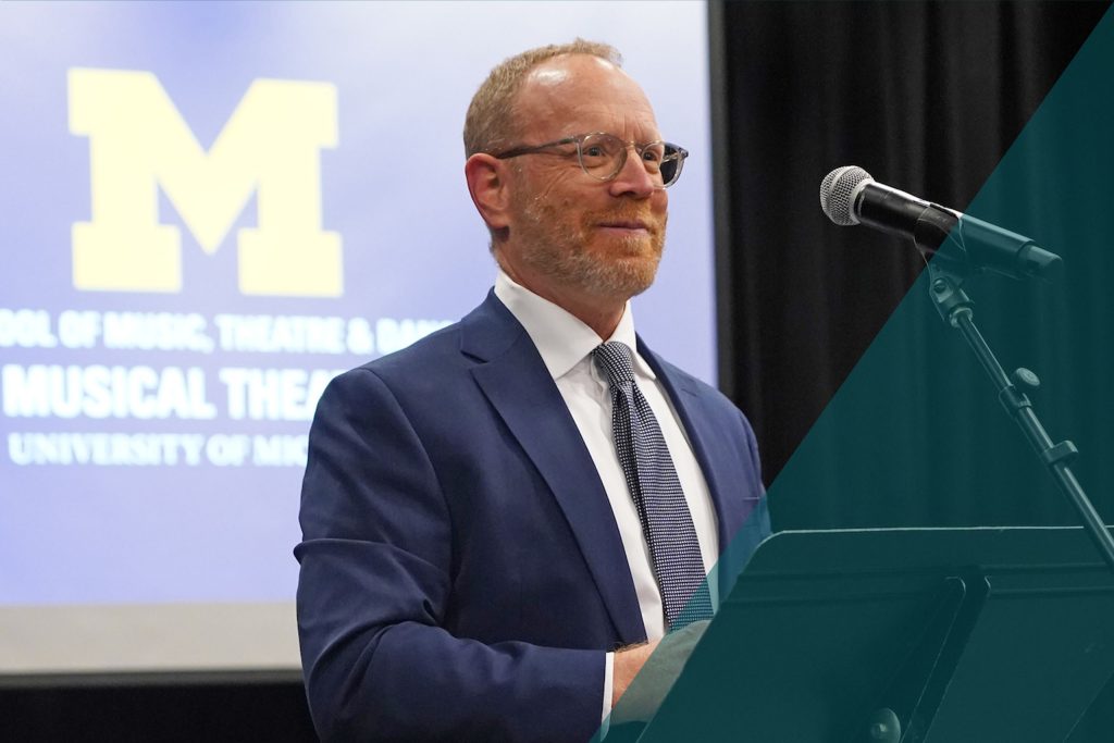 Dean David Gier stands at a microphone to speak at a Department of Musical Theatre event
