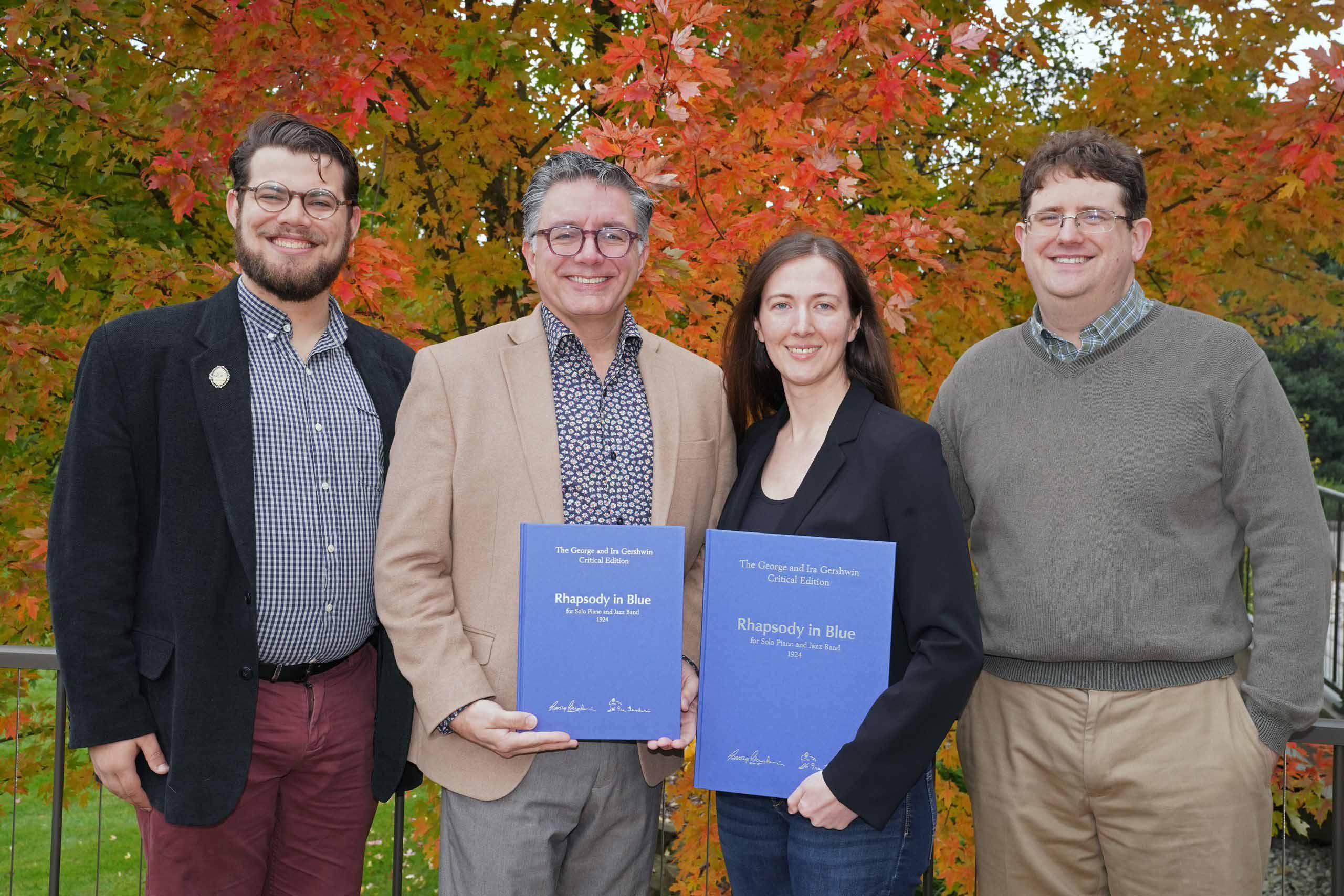 Four people pose outdoors, holding up two volumes with blue covers
