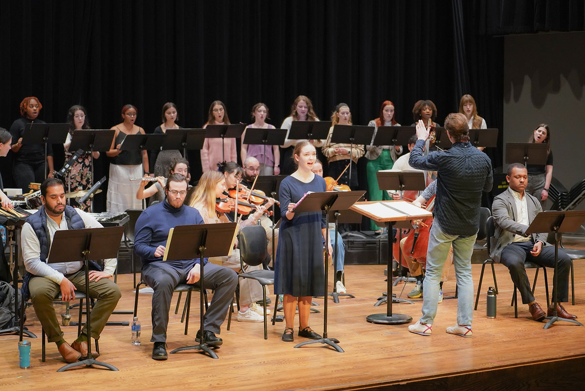 An instrumental ensemble, a choir and vocal soloists on stage in a rehearsal.