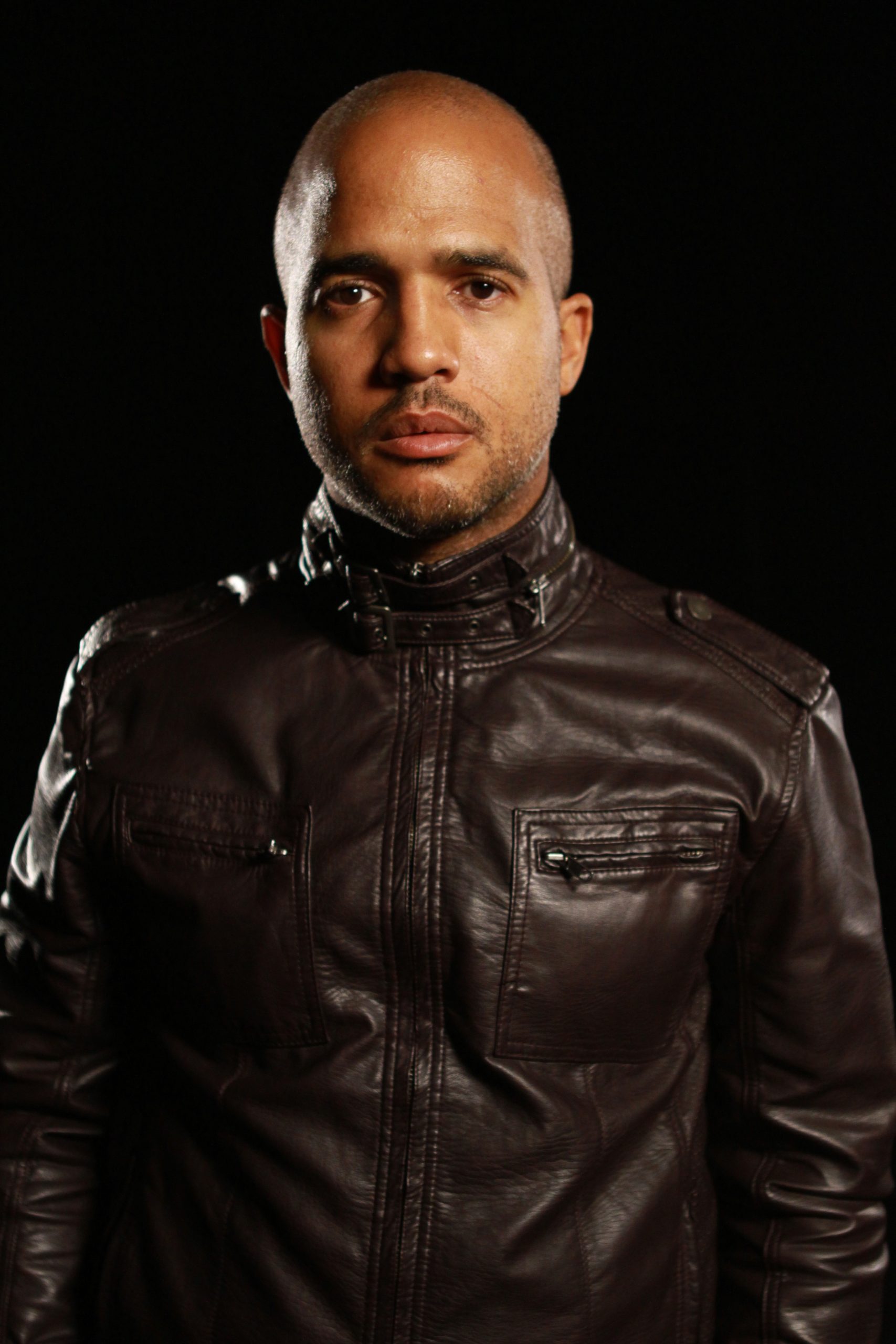 Studio headshot of Daniel Bernard Roumain wearing a black leather jacket, with black background