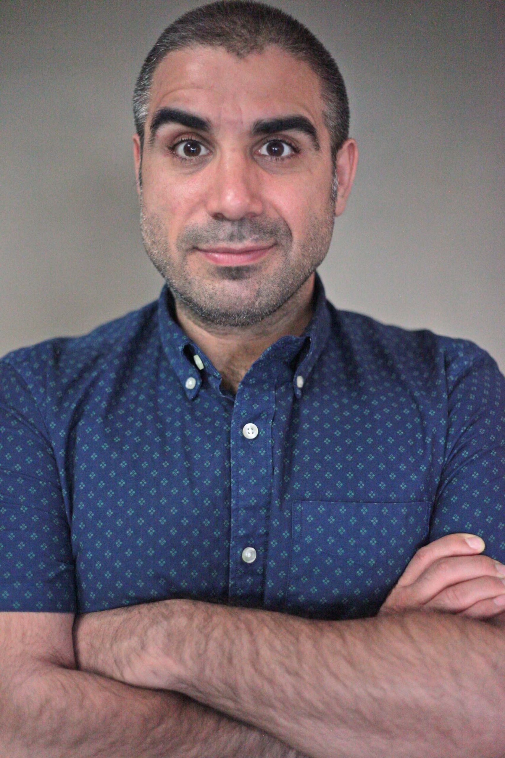 Mike Mosallam headshot with arms folded, wearing a dark blue collared shirt, grey background