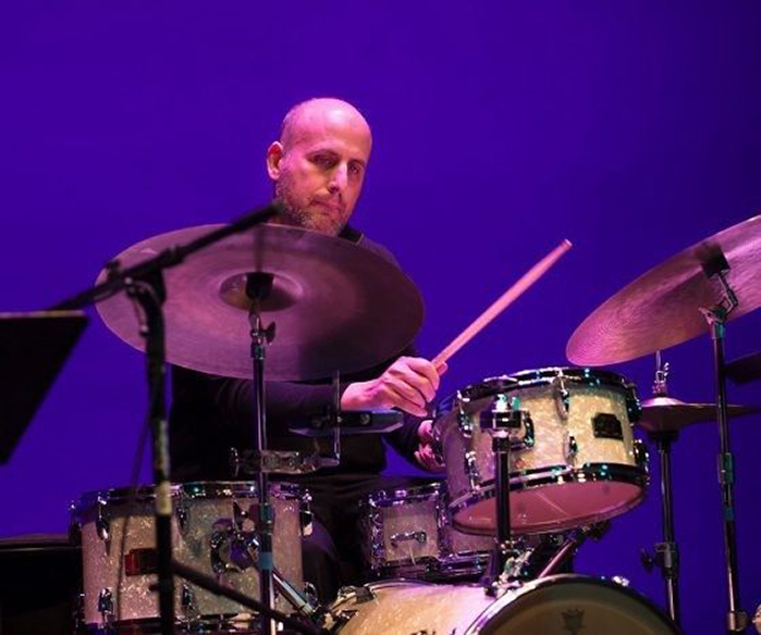 Michael Gould performs on a drumset under dark stage lighting