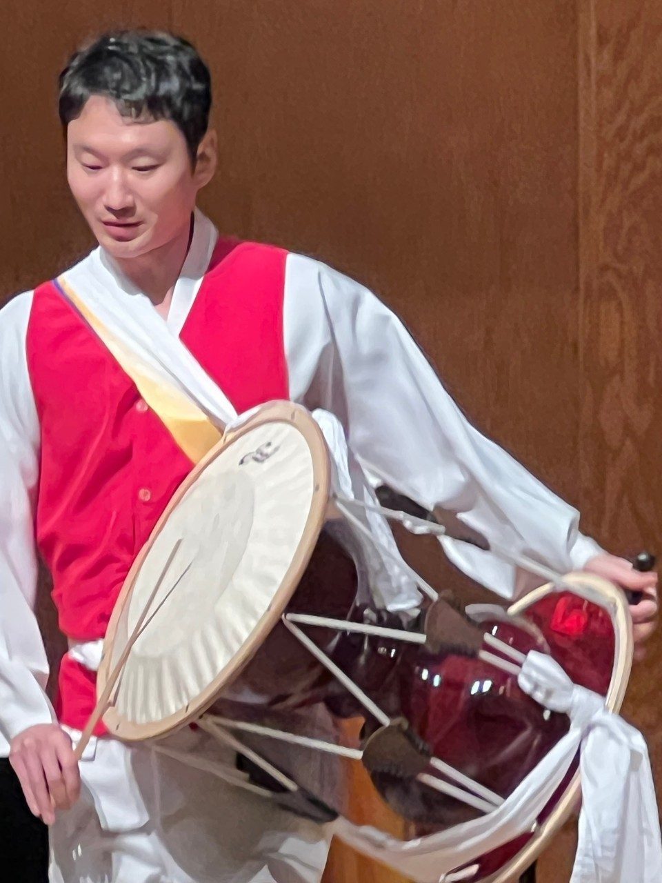 Suwan Choi performs standing, playing a drum strapped around the shoulder