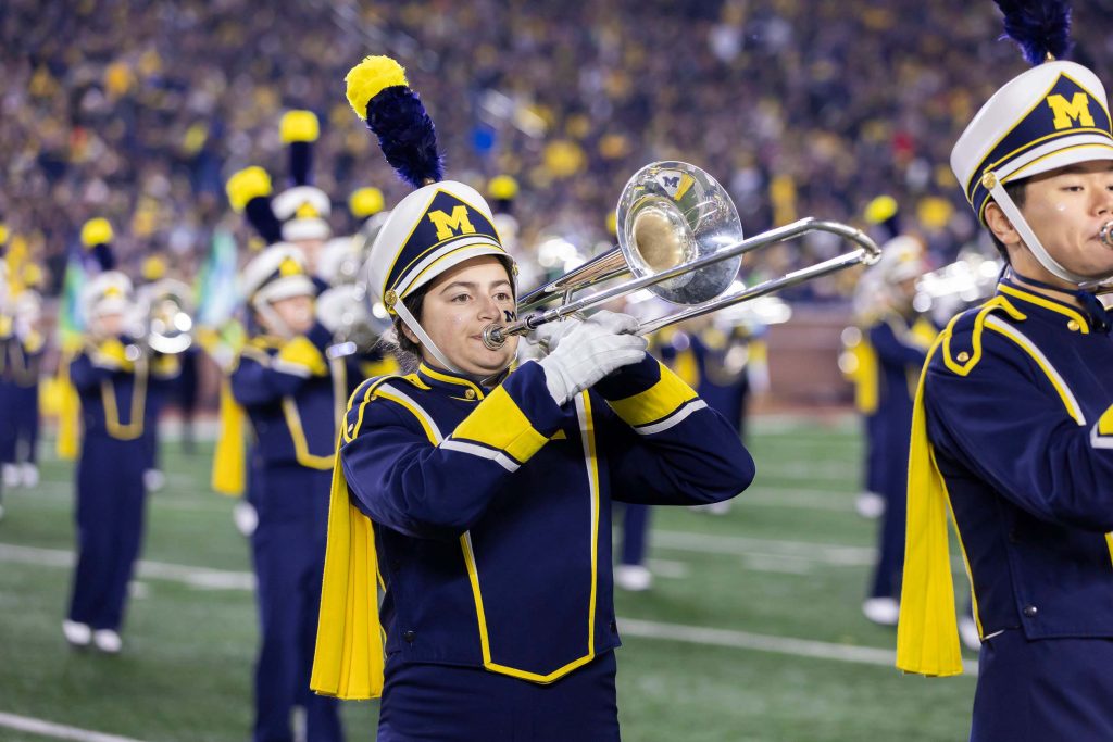 Aryn Nester performs on trombone on a football field in formation with the Michigan Marching Band
