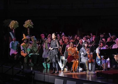 Graduate student conductor speaks to the audience from stage wearing a black costume