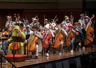 Rows of cello and double bass musicians perform on stage in Halloween costumes