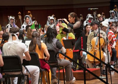 Graduate student conductor leads an orchestra on stage, all wearing costumes.