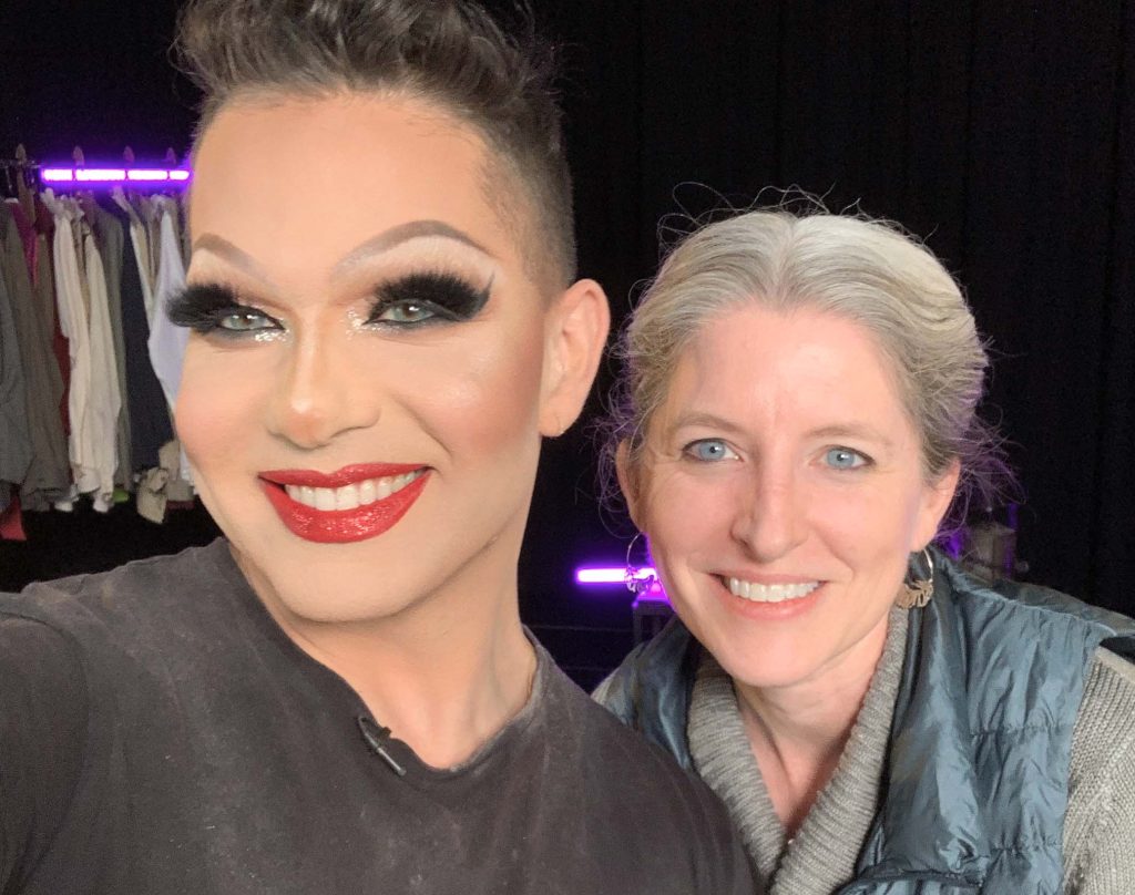 Student Alex Michaels, wearing theatrical makeup, poses smiling with Professor Sarah Oliver