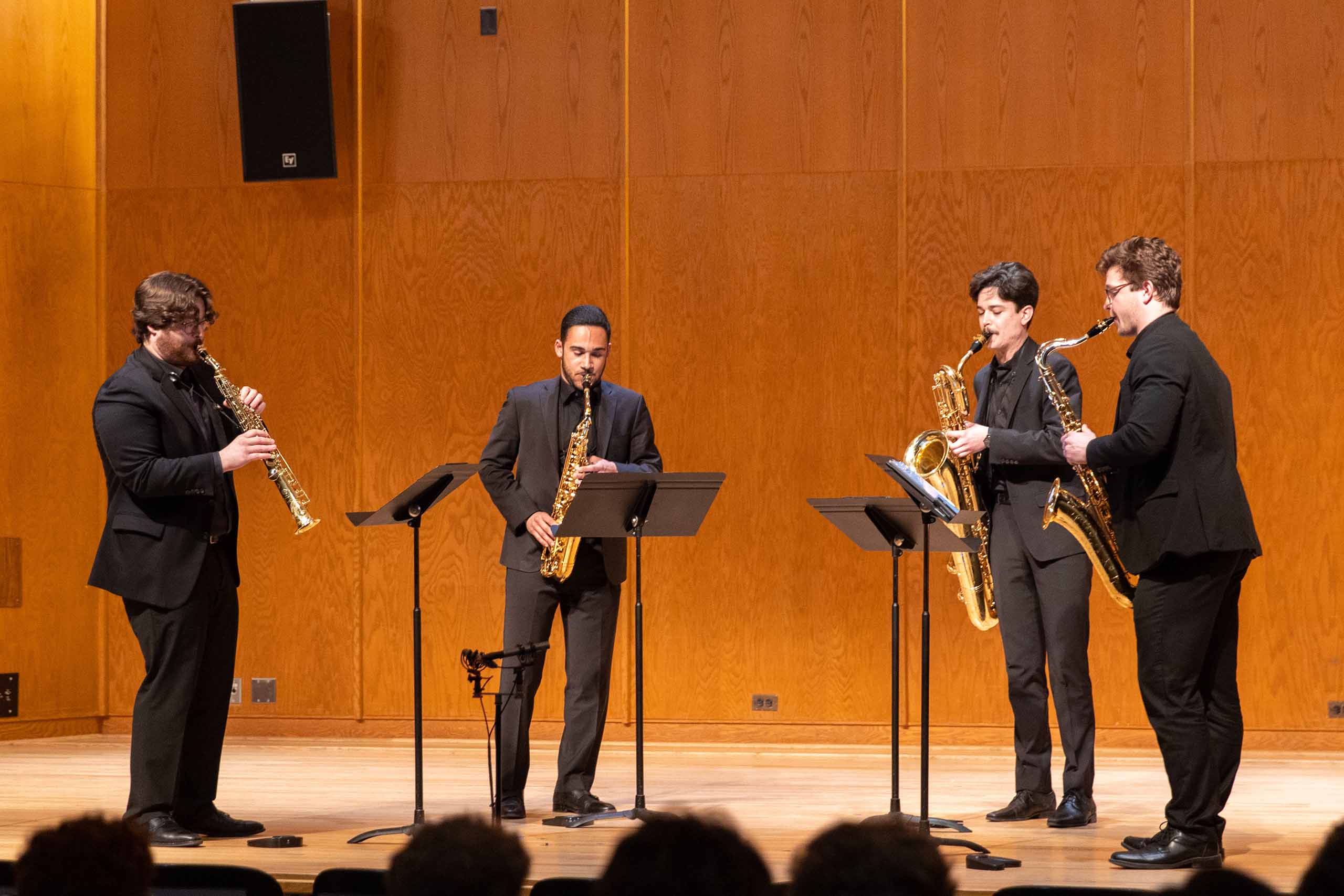 Quartet of saxophone players performs standing on stage, all dressed in black concert attire