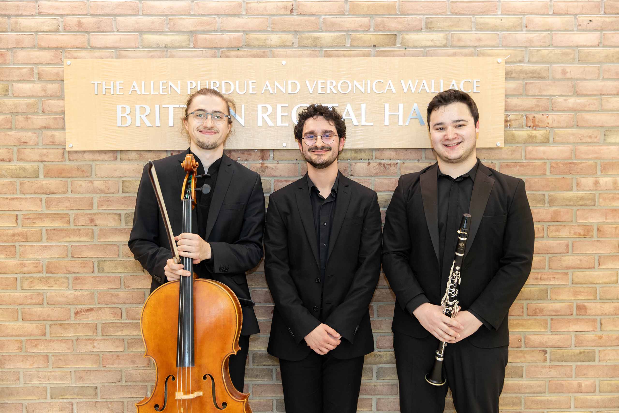 Trio poses standing outside Britton Recital Hall, holding instruments