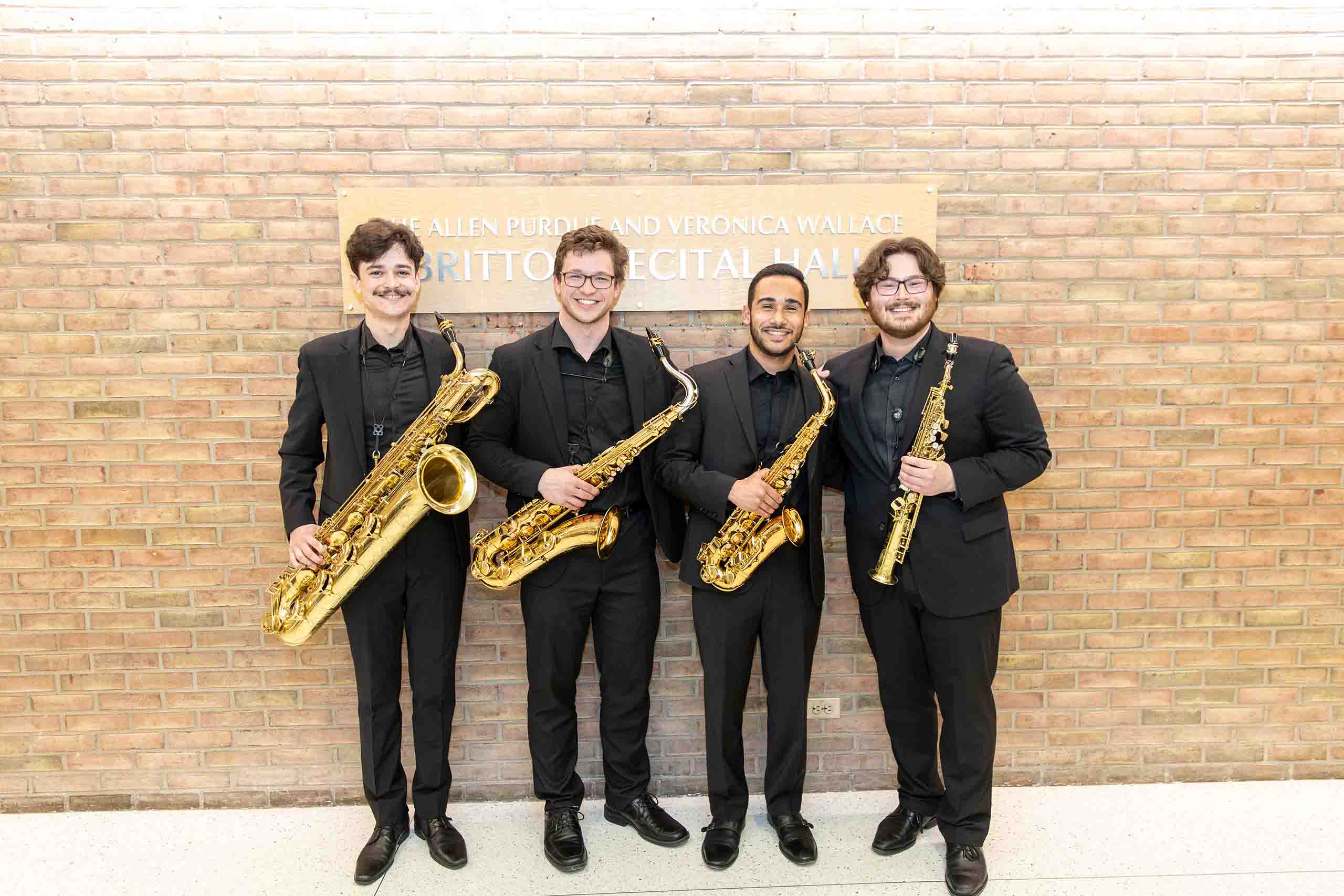 Trio poses standing outside Britton Recital Hall, holding instruments